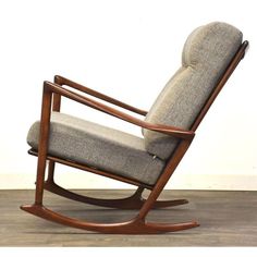 a rocking chair with grey upholstered fabric and wooden frame, in front of a white wall