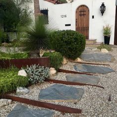 a house with stone steps leading up to the front door and side entrance, surrounded by greenery