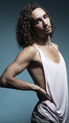 a man with long hair wearing a white tank top and gray pants is posing for the camera