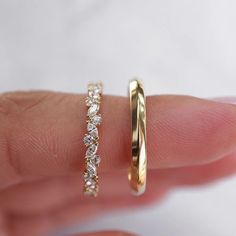 a woman's hand holding two wedding bands on her finger, with the band in gold