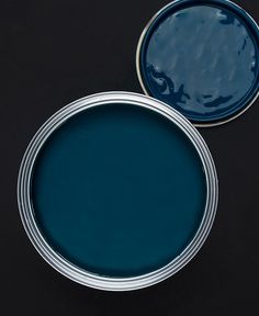 two tins with blue paint sitting on top of each other in front of a black background