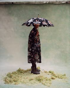 a woman holding an umbrella standing on top of a pile of dirt next to a wall