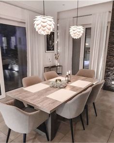 a dining room table with chairs and lights hanging from it's ceiling, in front of a large window