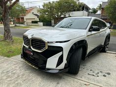 a white suv parked on the side of a road next to a tree and house