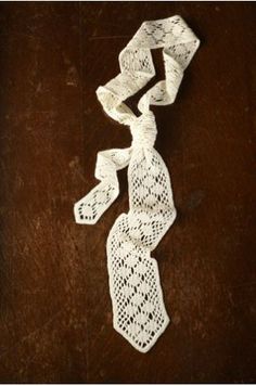 white crochet lace on wooden surface with knoted ends and two ties hanging from it