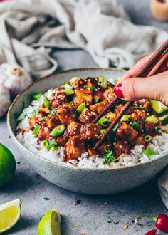 someone holding chopsticks over a bowl of rice with meat and vegetables on the side