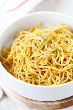 a white bowl filled with spaghetti on top of a wooden cutting board