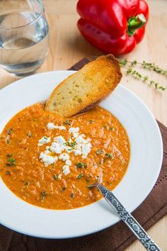 a bowl of soup with bread and cheese on the side sitting on a wooden table