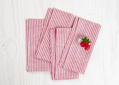 four red and white striped napkins with a single rose on the side, sitting on a white wooden surface