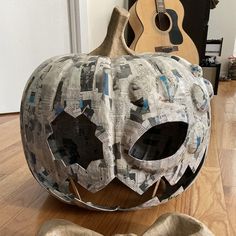 a paper mache pumpkin sitting on top of a wooden floor next to a guitar