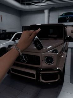 a hand pointing at a mercedes car in a showroom with other cars behind it