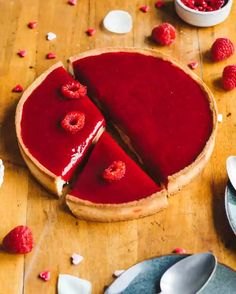 a raspberry cheesecake is cut into slices on a wooden table with spoons