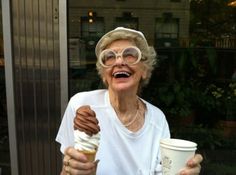 an older woman holding up a cup of ice cream and a chocolate covered donut