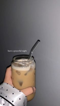 a hand holding a glass jar filled with liquid and a straw sticking out of it