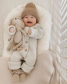 a baby is laying down with a stuffed animal in it's lap and wearing a knitted outfit