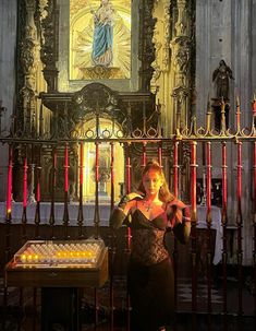 a woman standing in front of a church altar with candles on the table and an ornate alter behind her