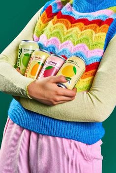 a woman holding three cans of juice in her hands and wearing a colorful sweater on