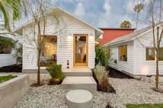 a white house with trees and bushes around it's front door, surrounded by gravel