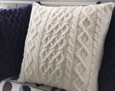 a white knitted pillow sitting on top of a blue and white couch next to a window