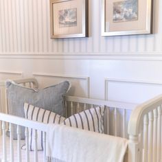 a white crib with two pictures on the wall above it and a blue striped pillow