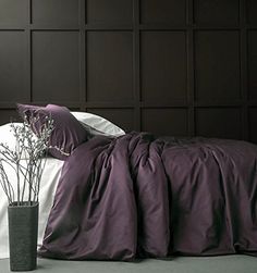 a bed with purple sheets and pillows on top of it next to a vase filled with flowers