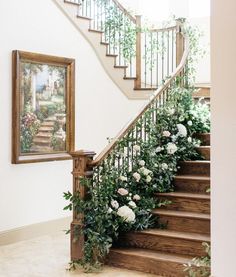 a staircase with white flowers and greenery on the bannister, next to a framed painting