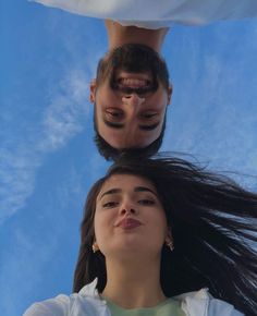 two people looking up at the sky with their hair blowing in the wind and one person holding his head