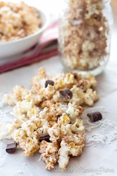 two bowls filled with popcorn and chocolate chips on top of a white table cloth next to a bowl of cereal