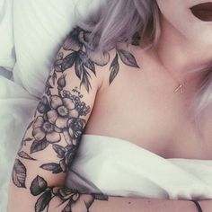 a woman laying in bed with tattoos on her arm