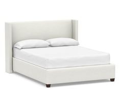 a white bed with two pillows on top of it and a night stand next to it