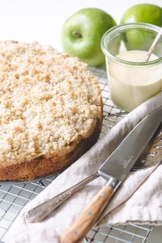 a cake sitting on top of a cooling rack next to two green apples and a knife