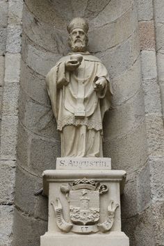 a statue of saint anthony in front of a stone wall with a coat on it