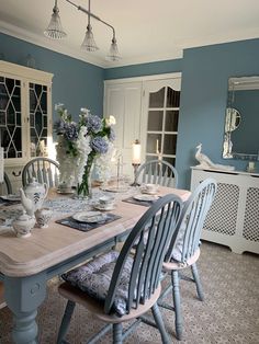 a dining room with blue walls and white furniture in the center, along with flowers on the table