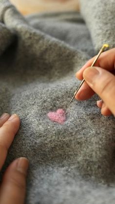 a woman is stitching a heart on a gray sweater with a needle and thread