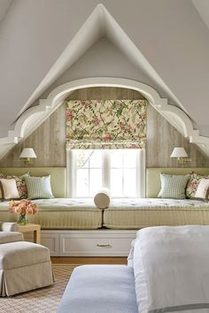 a bed sitting under a window in a bedroom next to a white chair and ottoman