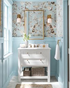 a bathroom with blue walls and floral wallpaper on the walls, along with a gold framed mirror