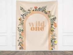 a wall hanging with the words wild one on it and flowers around it in front of a wooden floor