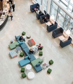 an overhead view of people sitting at tables and couches in a lobby with large windows