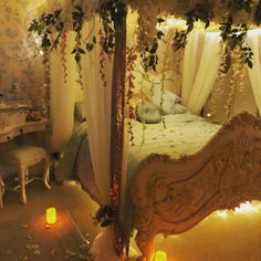 a canopy bed in a bedroom with candles on the floor and curtains hanging from the ceiling