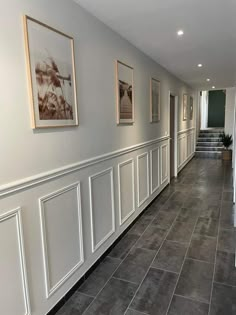 a long hallway with white paneling and pictures on the wall next to each other