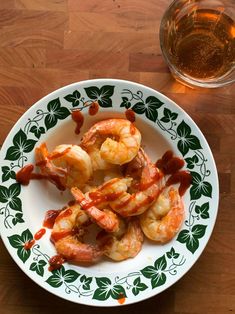 shrimp with sauce on a plate next to a glass of beer and a wooden table