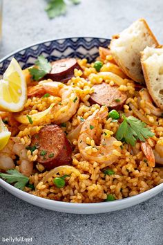 a bowl filled with rice and shrimp on top of a table next to lemon wedges