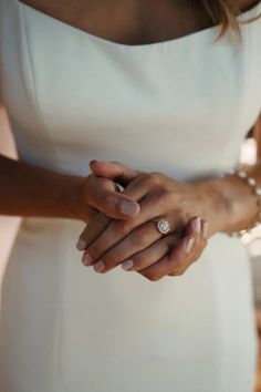 a woman in a white dress holding her wedding ring and wearing a pearled bracelet