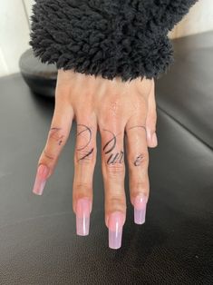 a woman's hand with pink nails and tattoos on her left thumb, sitting on a black surface