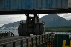 a large truck driving across a bridge next to a body of water with a boat in the background