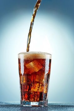 a drink being poured into a glass filled with ice cubes on a blue background