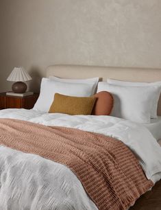 a bed with pillows and blankets on top of it in front of a wall mounted lamp