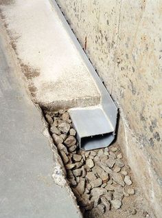 a cement wall with a pipe sticking out of it's side next to a sidewalk