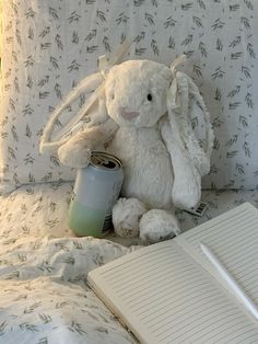 a white stuffed animal sitting on top of a bed next to an open book and pen