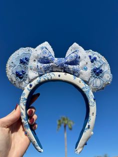 a person holding up a blue and white mickey ears headband in front of a palm tree